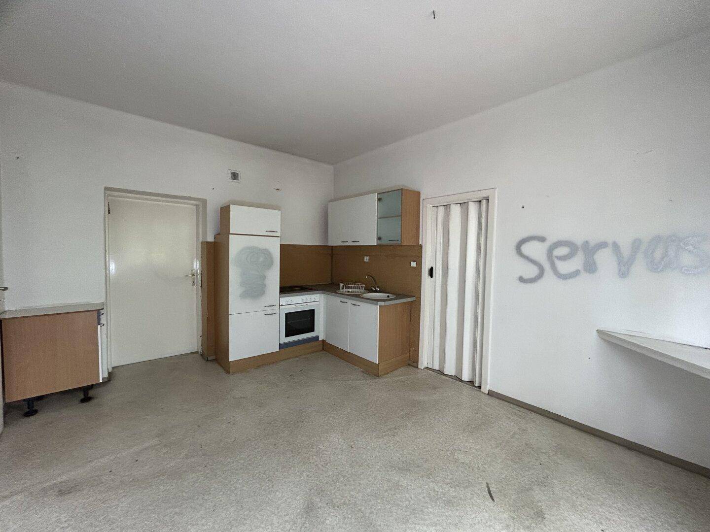 Kleine Küche mit einfacher Einbauküche, Herd und Spüle, mit Graffiti an der Wand.