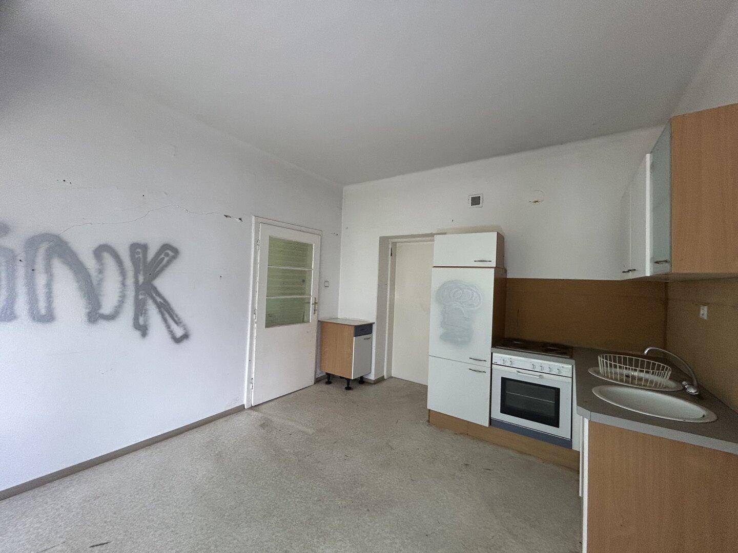 Kleine Küche mit einfacher Einbauküche, Herd und Spüle, mit Graffiti an der Wand.
