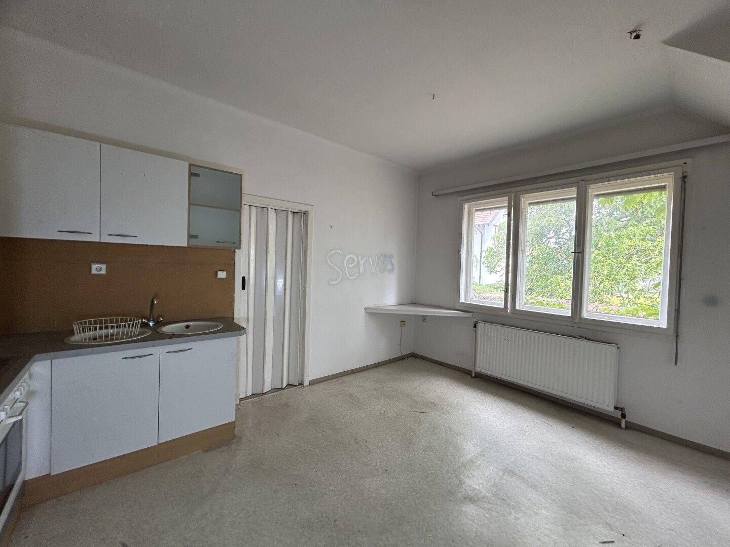 Kleine Küche mit einfacher Einbauküche, Fenster und Heizkörper, mit Blick ins Grüne.