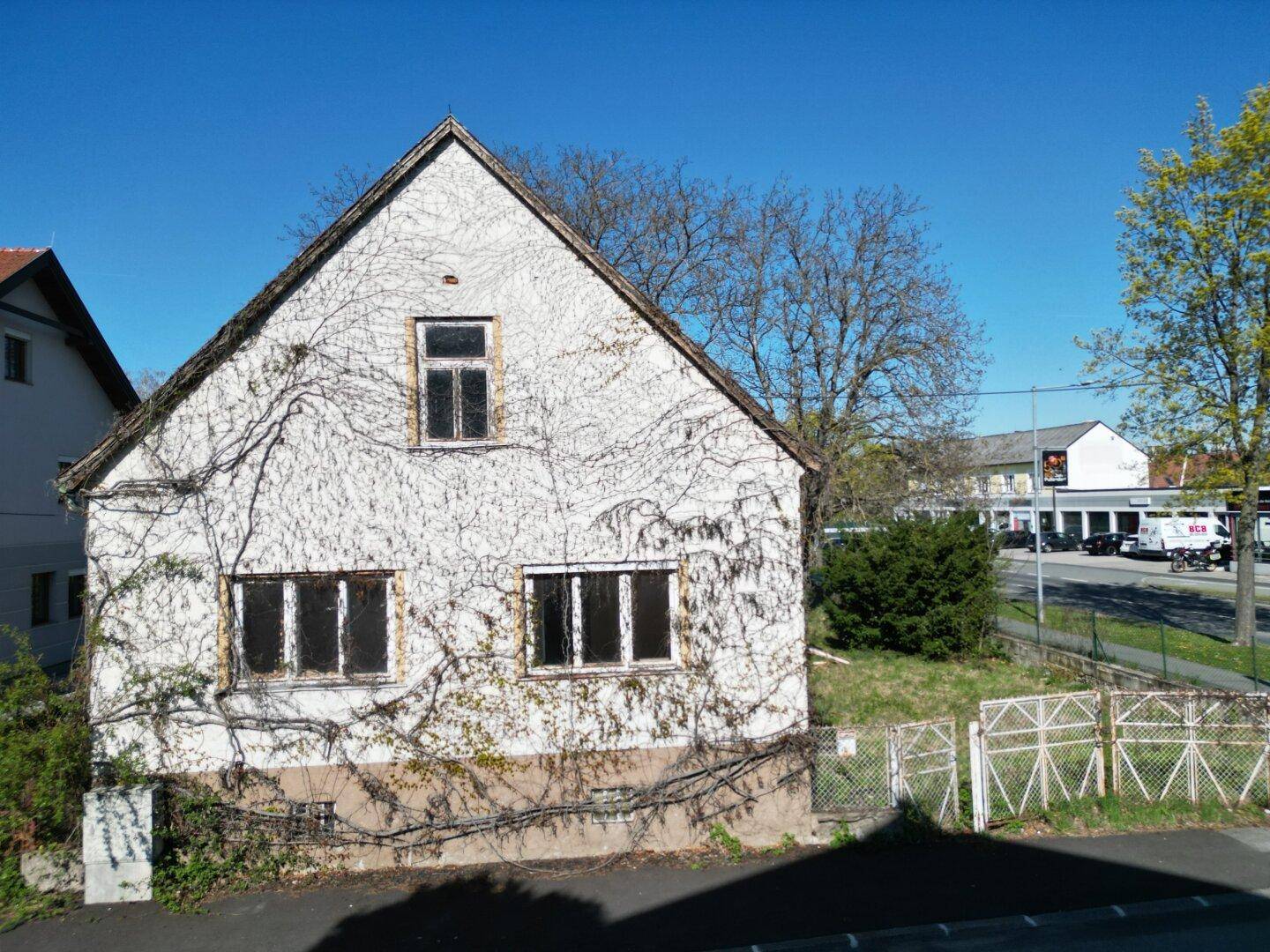 Vorderansicht eines älteren Hauses mit kahlen Ranken an der Fassade und Blick auf die Straße.
