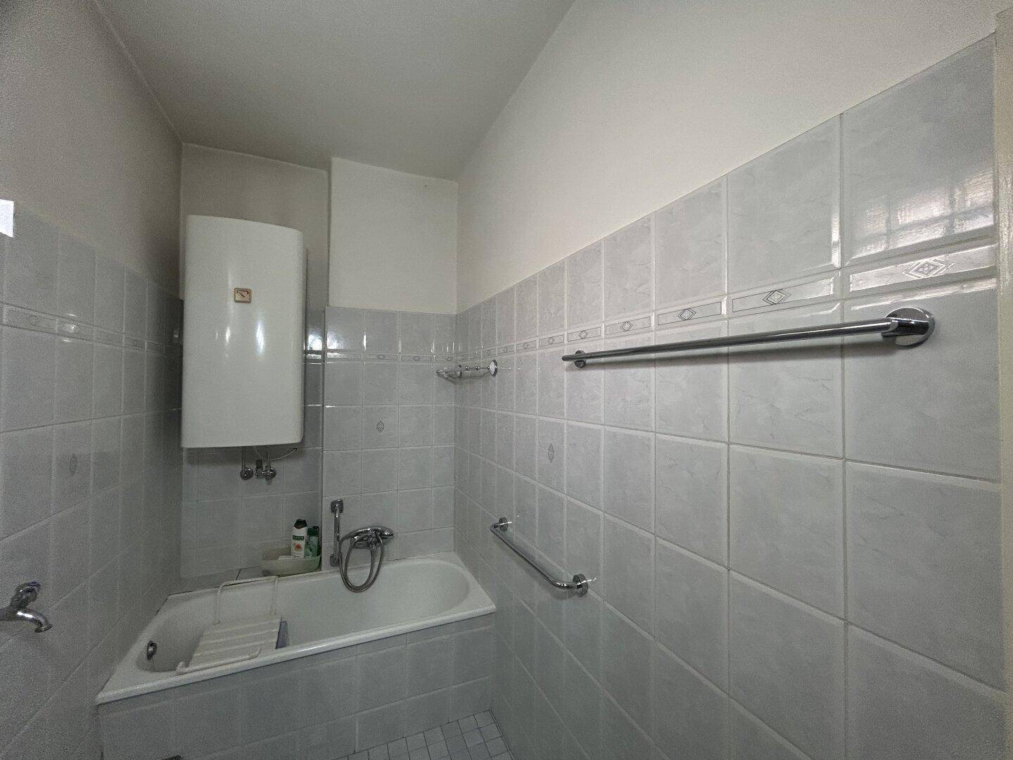 Badezimmer mit Badewanne, Fliesen an den Wänden und einem Warmwasserboiler.