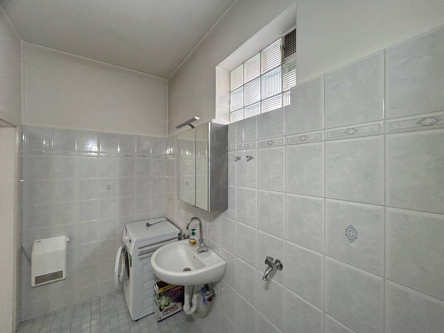 Badezimmer mit Waschbecken, Waschmaschine und Fliesenwänden, funktional eingerichtet.