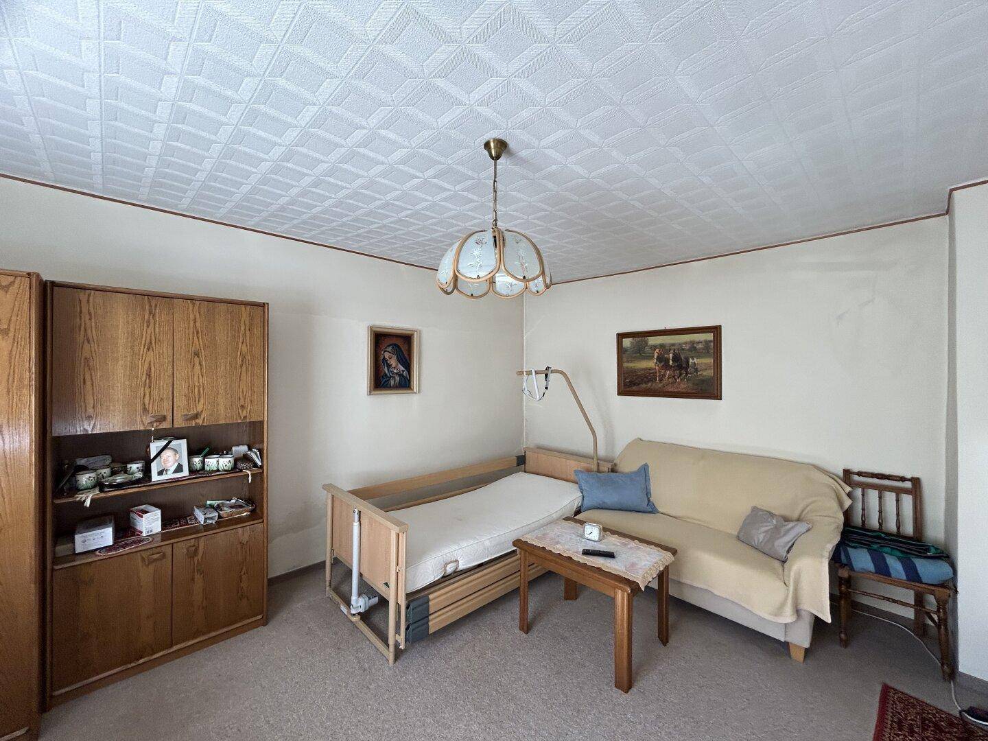 Schlafzimmer mit Bett, Sofa und Schrank, ausgestattet mit Teppichboden und Deckenpaneelen.