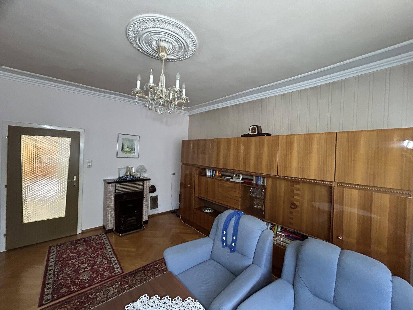Geräumiges Wohnzimmer mit Kronleuchter, Kaminofen und Holzparkettboden, klassisch eingerichtet.