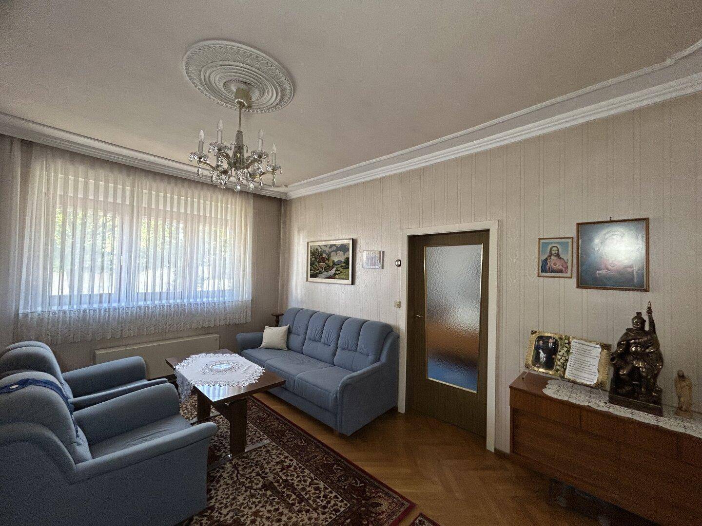 Helles Wohnzimmer mit Sofa, Kronleuchter und großem Fenster, bietet viel Tageslicht.