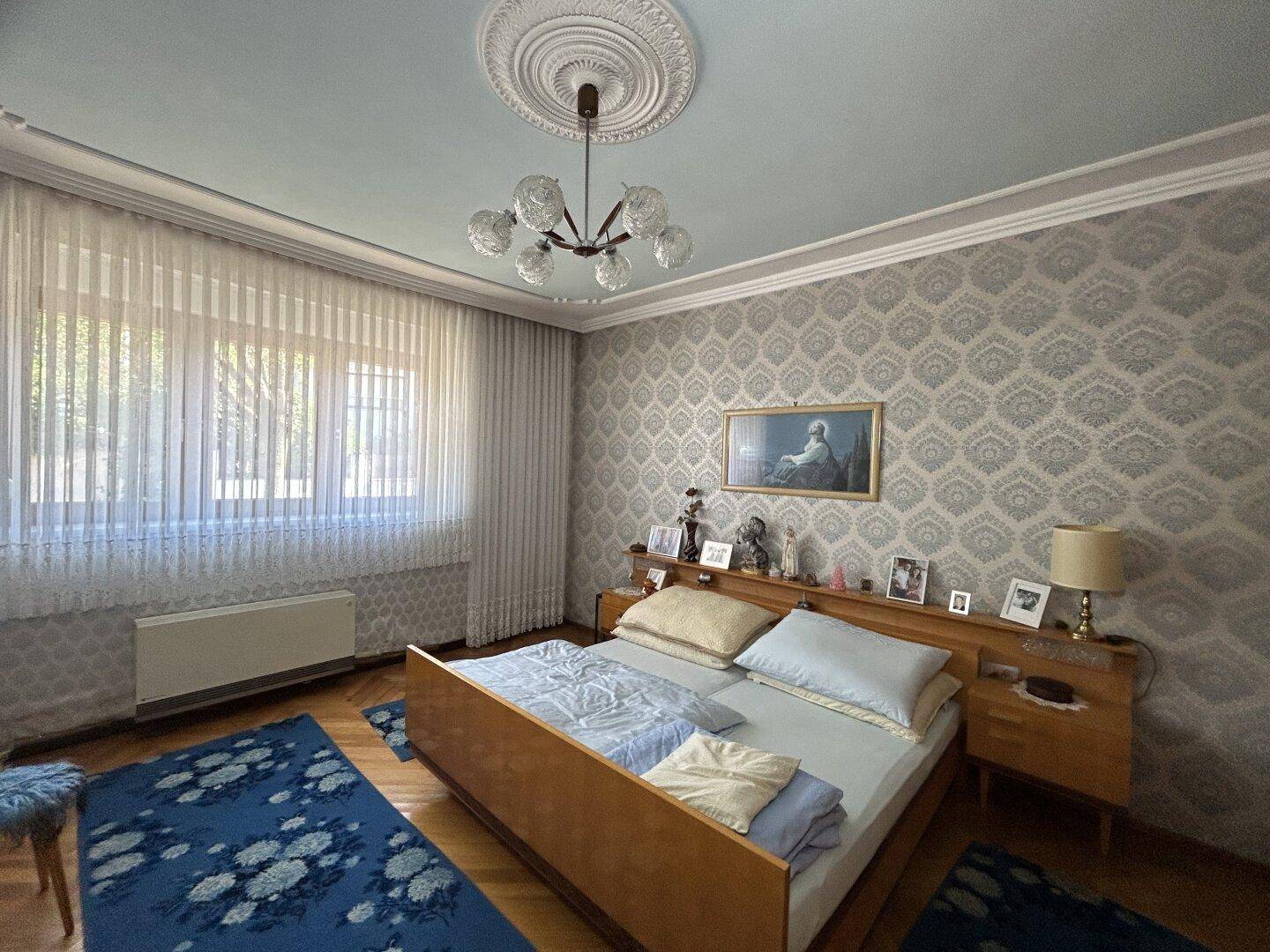 Schlafzimmer mit Doppelbett, gemusterter Tapete und Holzparkettboden, klassisch eingerichtet.