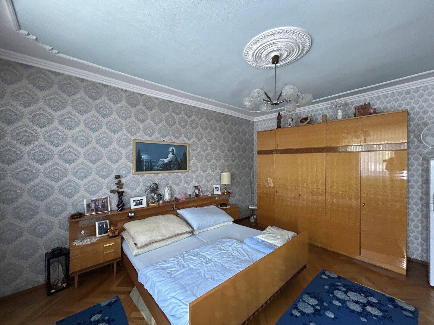Schlafzimmer mit Doppelbett, großem Kleiderschrank und gemusterter Tapete, funktional eingerichtet.