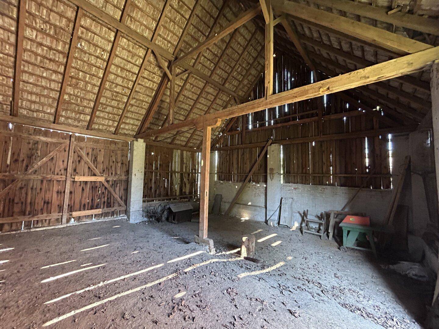Großer, leerer Scheunenraum mit sichtbaren Holzbalken und viel natürlichem Lichteinfall.