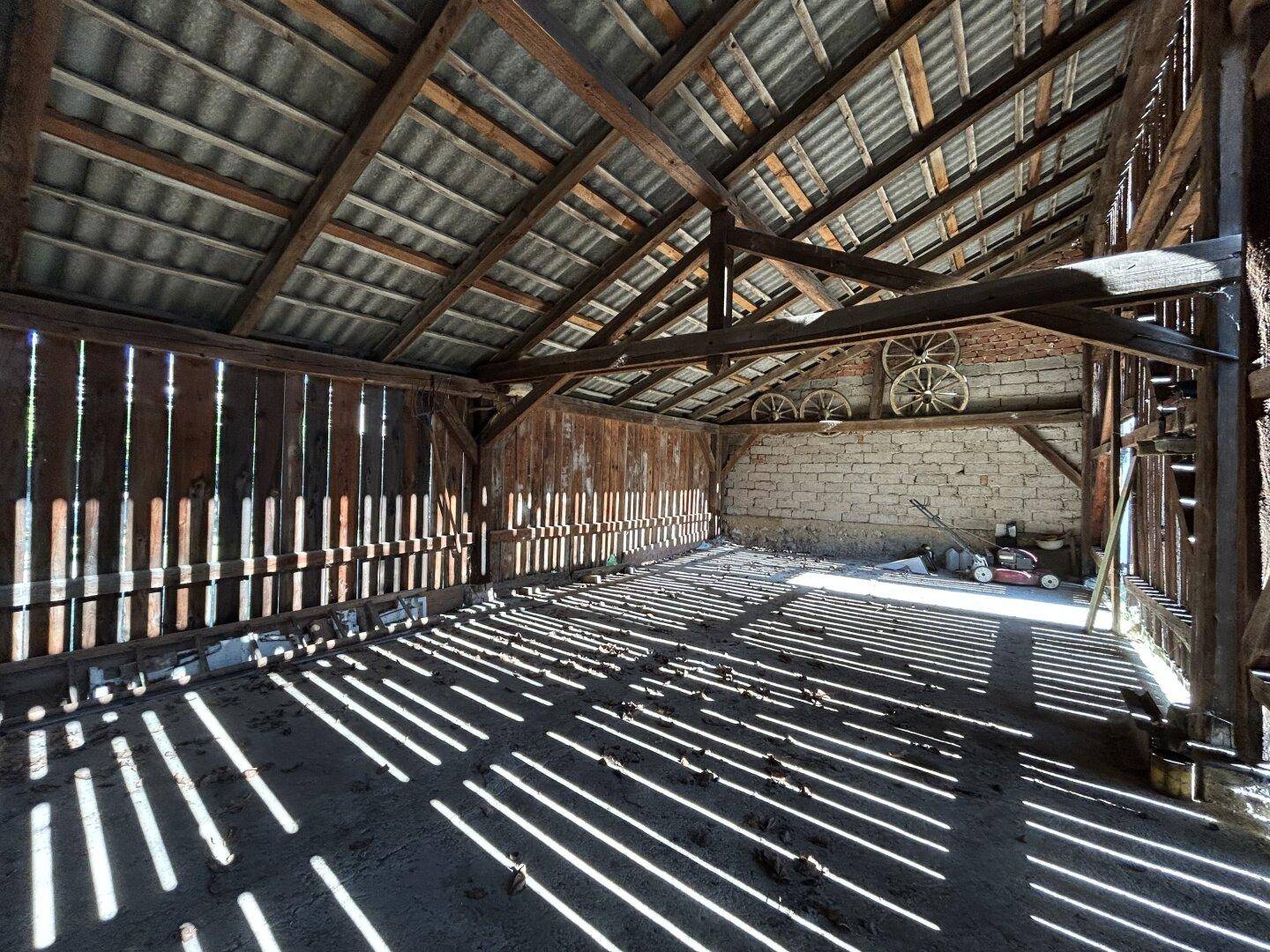 Rustikaler Scheuneninnenraum mit Holzbalken, alten Wagenrädern und natürlichem Lichteinfall.