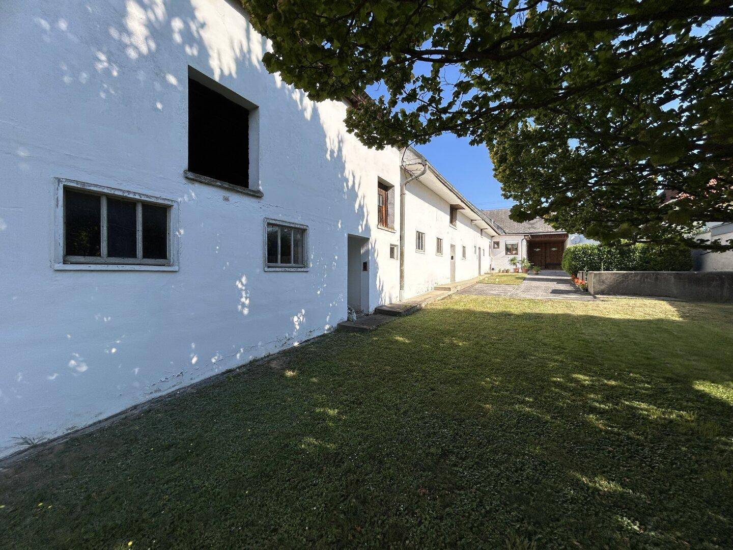 Lange weiße Fassade eines alten Gebäudes mit Fenstern und Türen, umgeben von Rasen.
