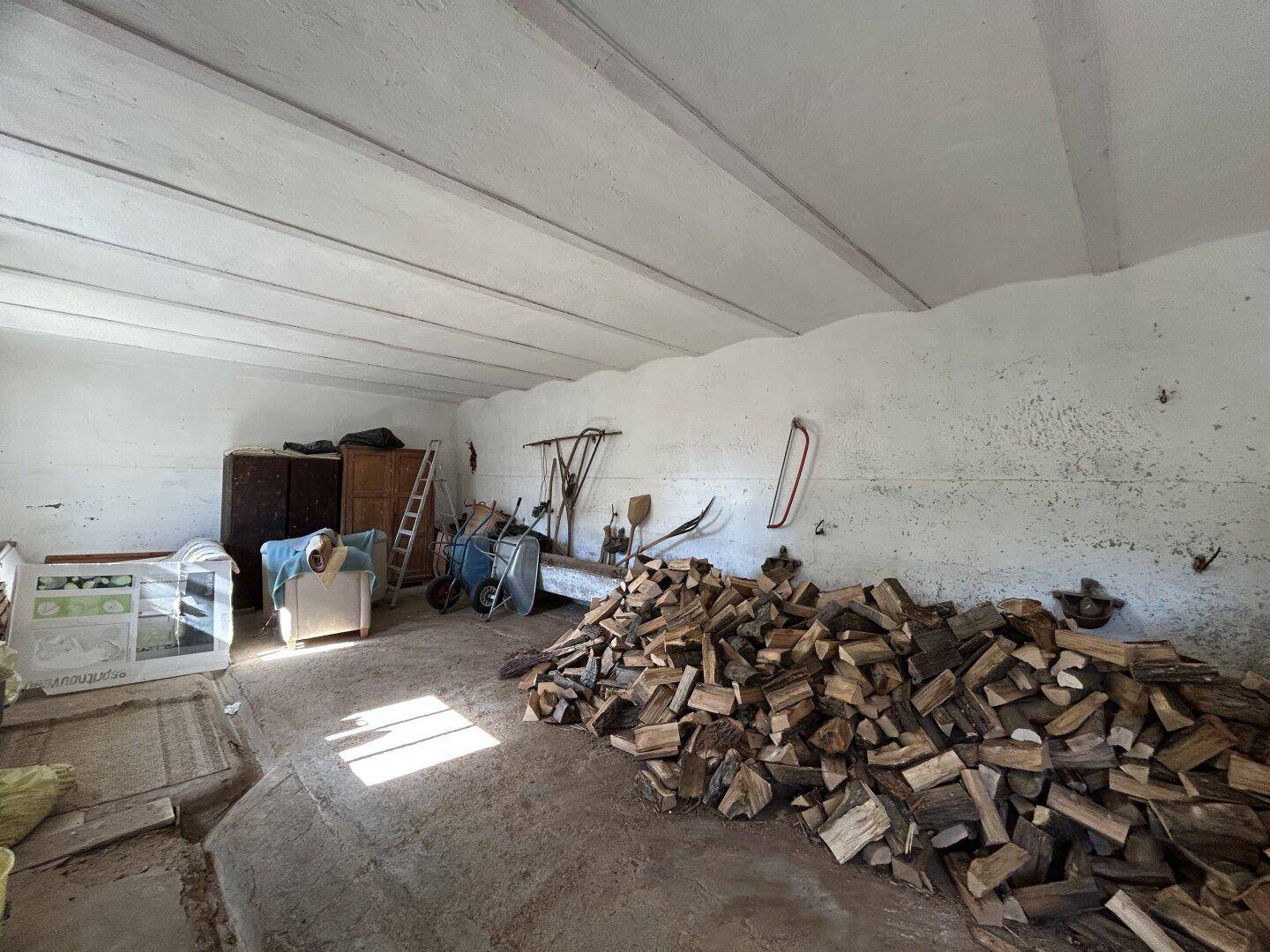 Lagerraum mit Holzbalkendecke, gestapeltem Brennholz und verschiedenen Geräten.