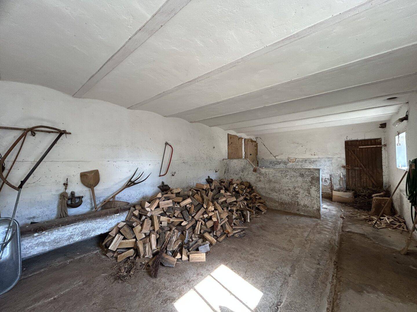 Rustikaler Lagerraum mit Holzbalkendecke, Brennholzstapel und alten Werkzeugen.