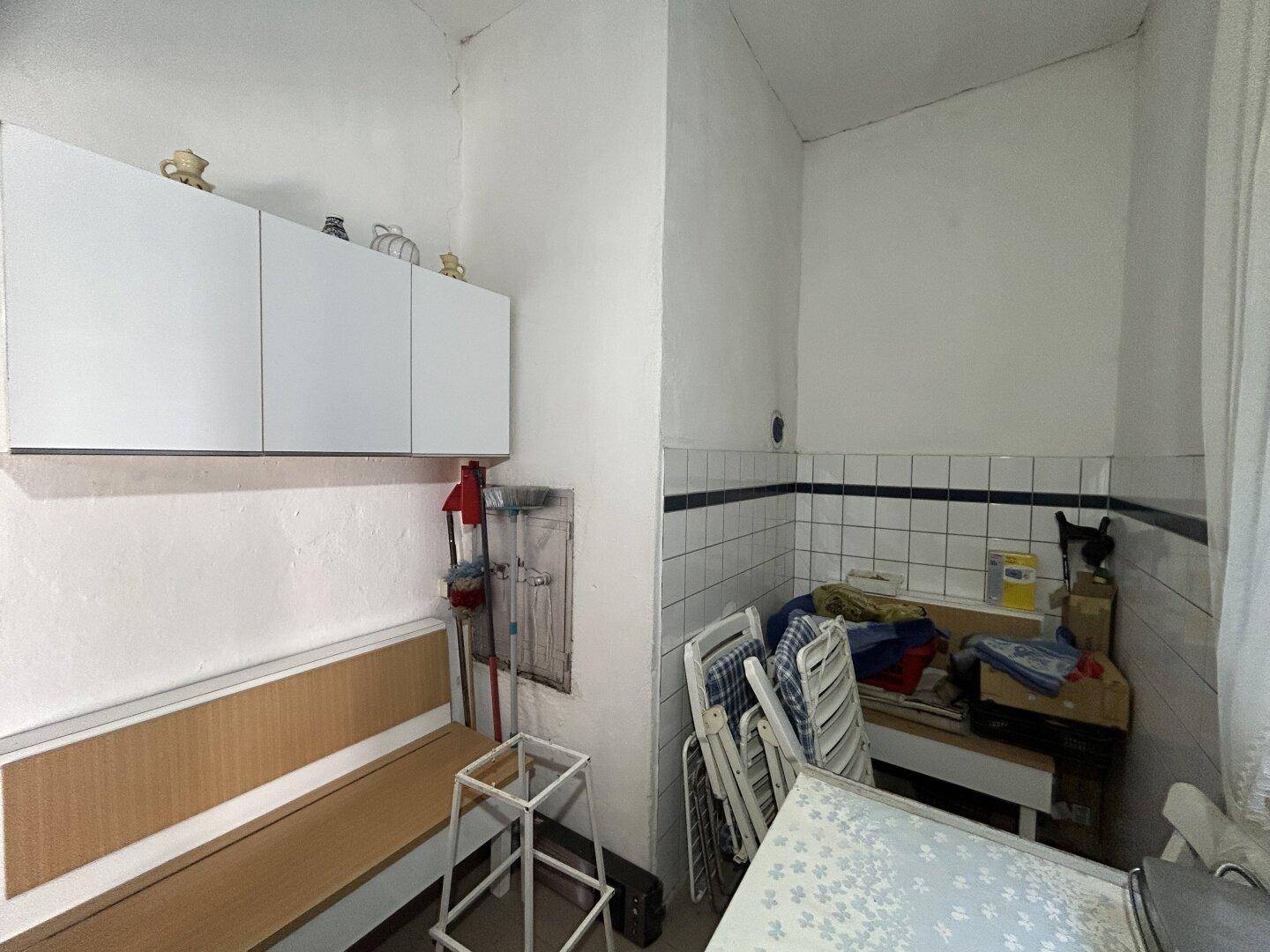 Kleiner Abstellraum mit Fliesenwand, Hängeschränken und Klappstühlen.