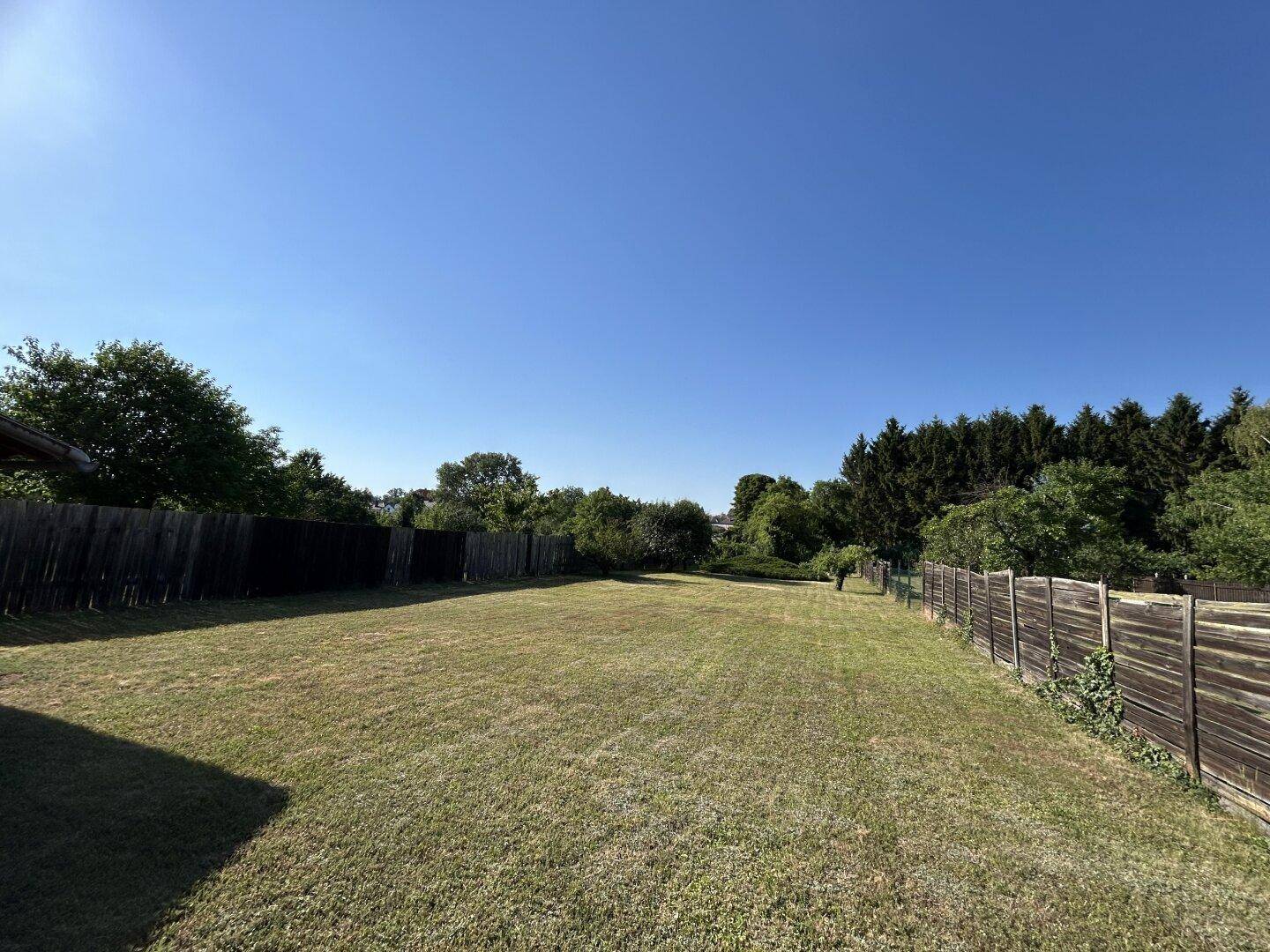 Ausgedehnter Gartenbereich mit Rasen, Holzzaun und Blick auf die umliegende Natur.