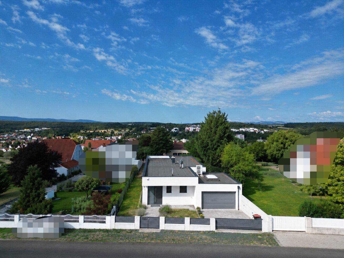 Freistehendes modernes Haus mit Flachdach und Garage, umgeben von Gärten und ländlicher Weite.