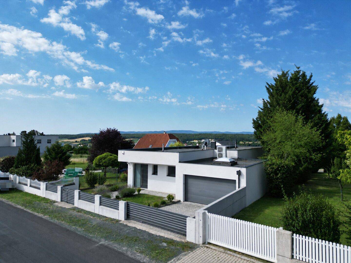 Zeitgenössisches Einfamilienhaus mit Flachdach und integrierter Garage, umgeben von viel Grün.