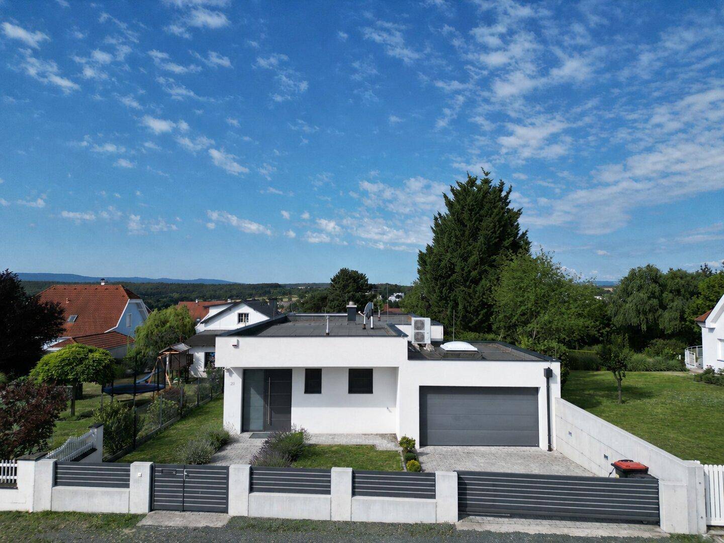 Modernes Wohnhaus mit weißer Fassade, Flachdach und Garage, eingebettet in eine grüne Landschaft.