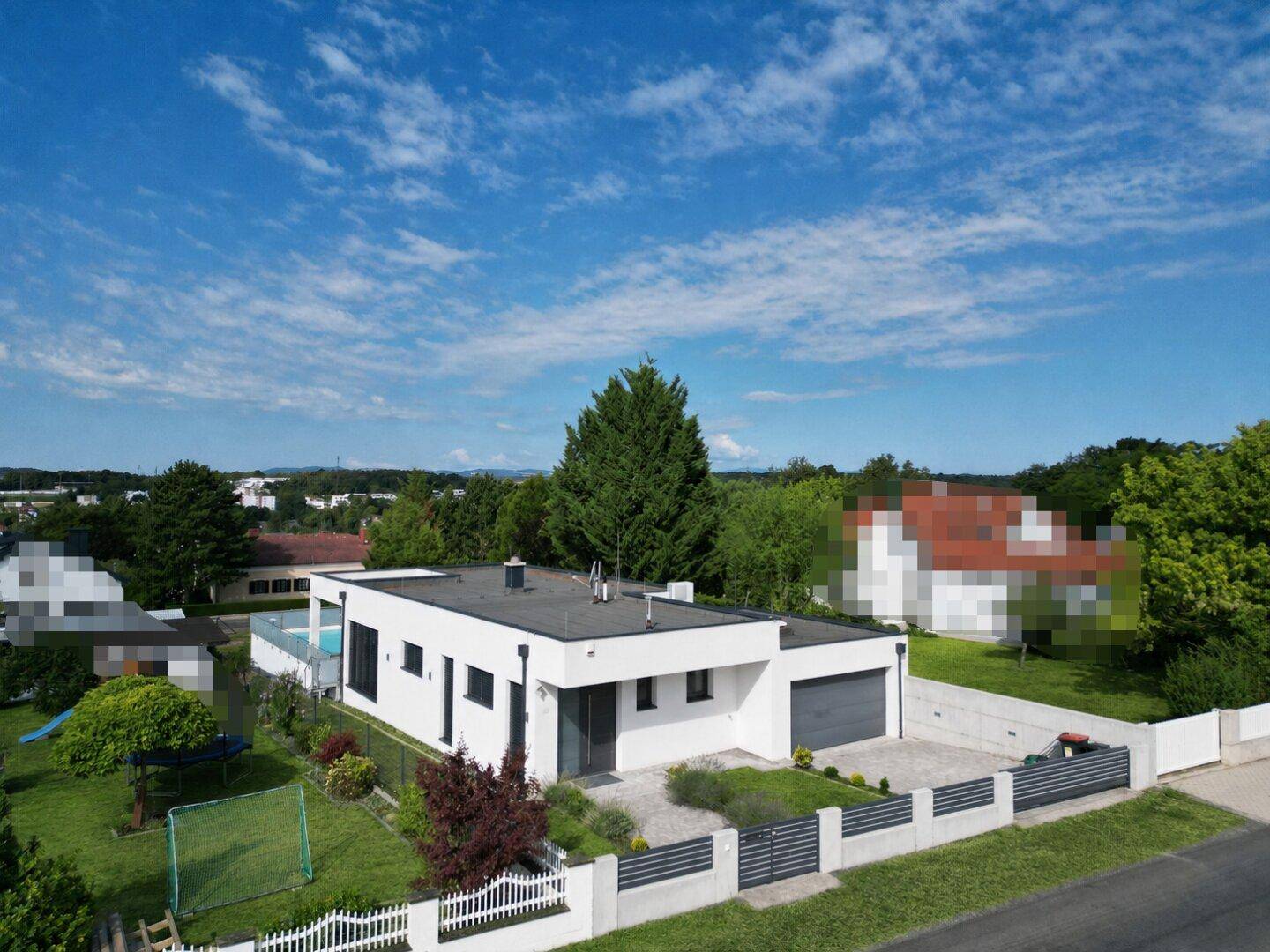 Moderne weiße Villa mit Flachdach, Pool und gepflegtem Garten in ländlicher Umgebung.