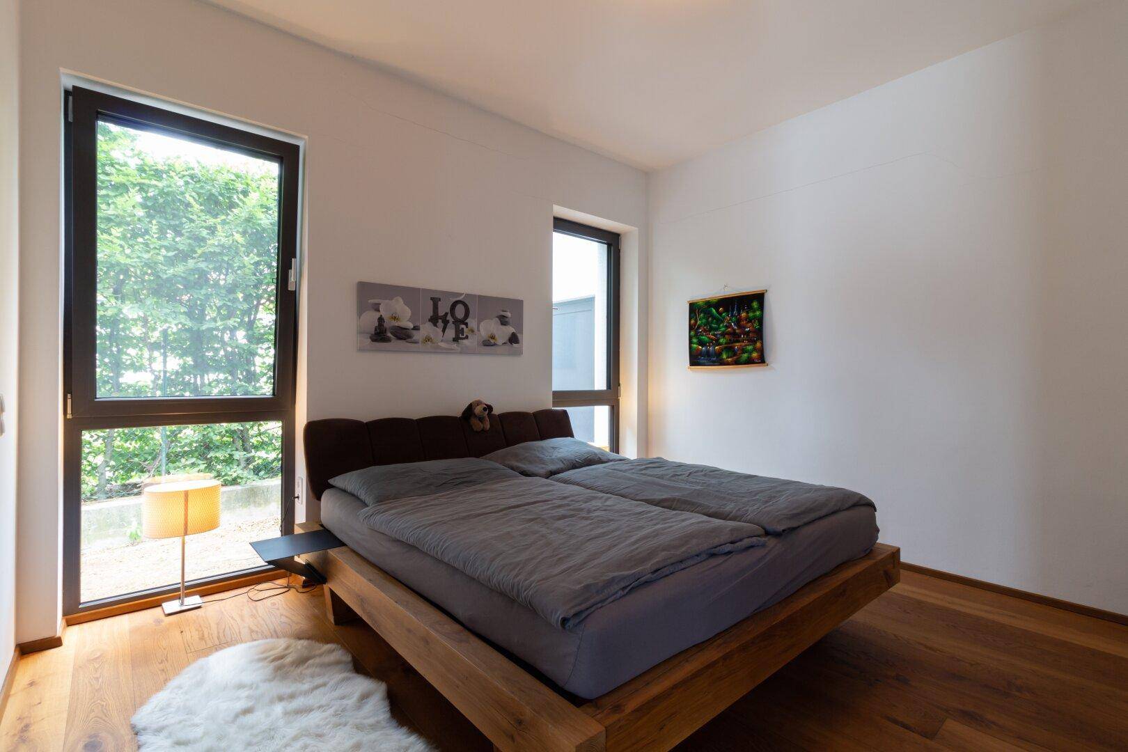 Schlafzimmer mit Holzbett, Holzboden und großen Fenstern mit Blick ins Grüne.