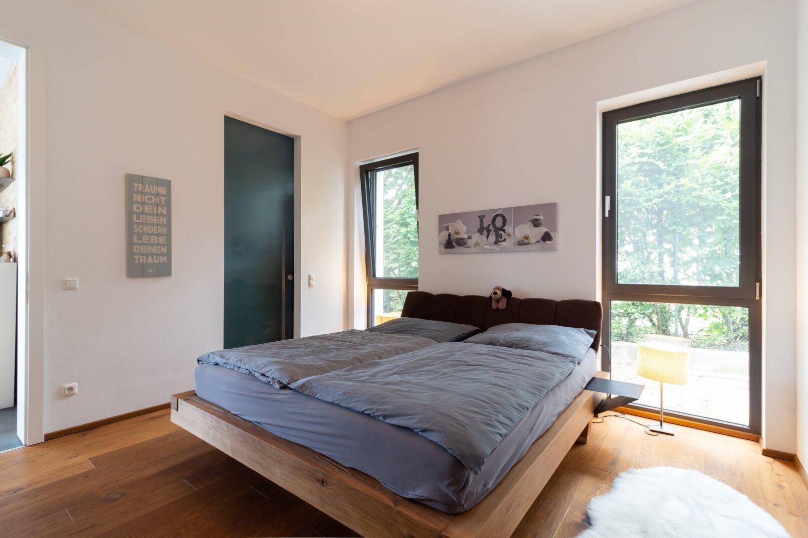 Helles Schlafzimmer mit Holzboden, großen Fenstern und minimalistischer Einrichtung.