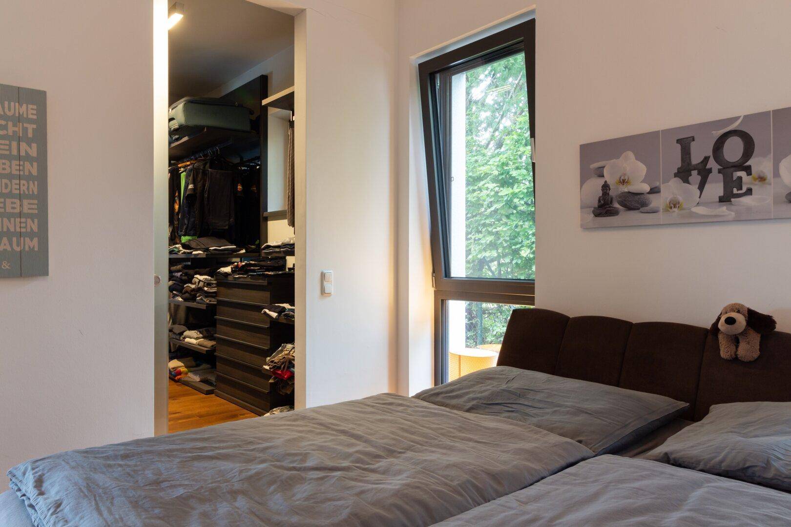 Schlafzimmer mit Holzboden und Blick auf den angrenzenden begehbaren Kleiderschrank.