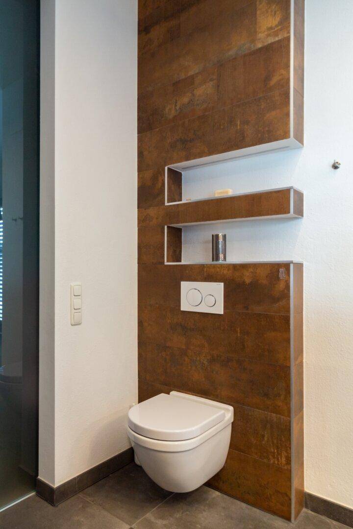 Modernes wandhängendes WC mit stilvollen Holzoptikfliesen und integrierten Ablagen.