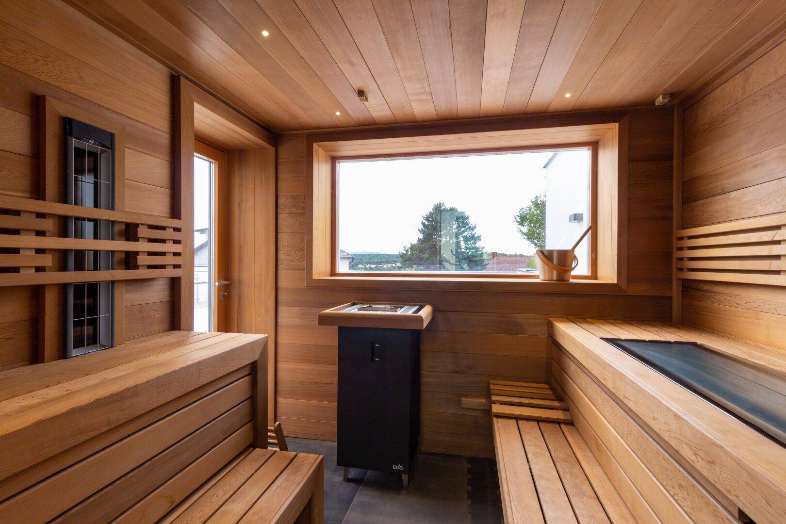Gemütliche Holzsauna mit breiten Bänken, Saunaofen und einem Fenster mit Ausblick.