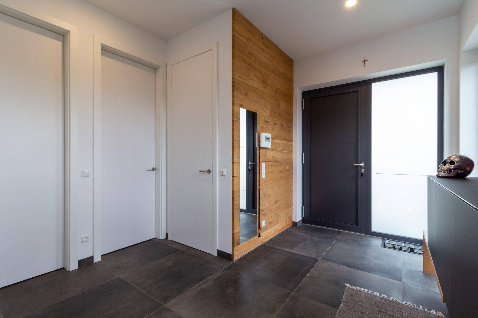 Geräumiger Flur mit dunklen Fliesen, Holzwandverkleidung und modernen weißen Türen.