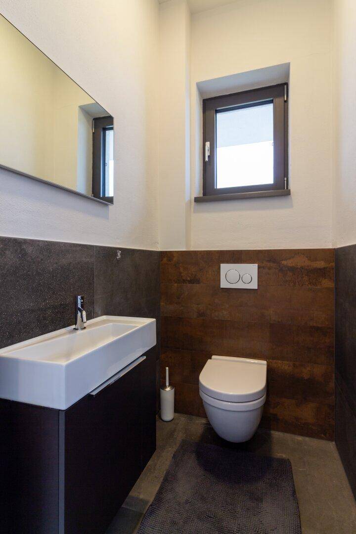Modernes Gäste-WC mit elegantem Waschtisch, Spiegel und einem Fenster für Tageslicht.