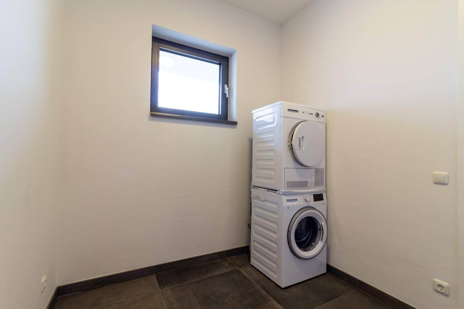 Praktischer Hauswirtschaftsraum mit gestapelter Waschmaschine und Trockner sowie einem Fenster.