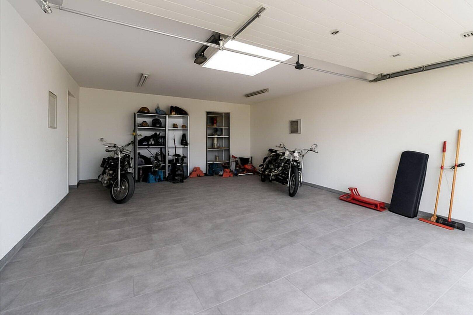 Geräumige Garage mit Fliesenboden, Regalen und Platz für Fahrzeuge und Motorräder.