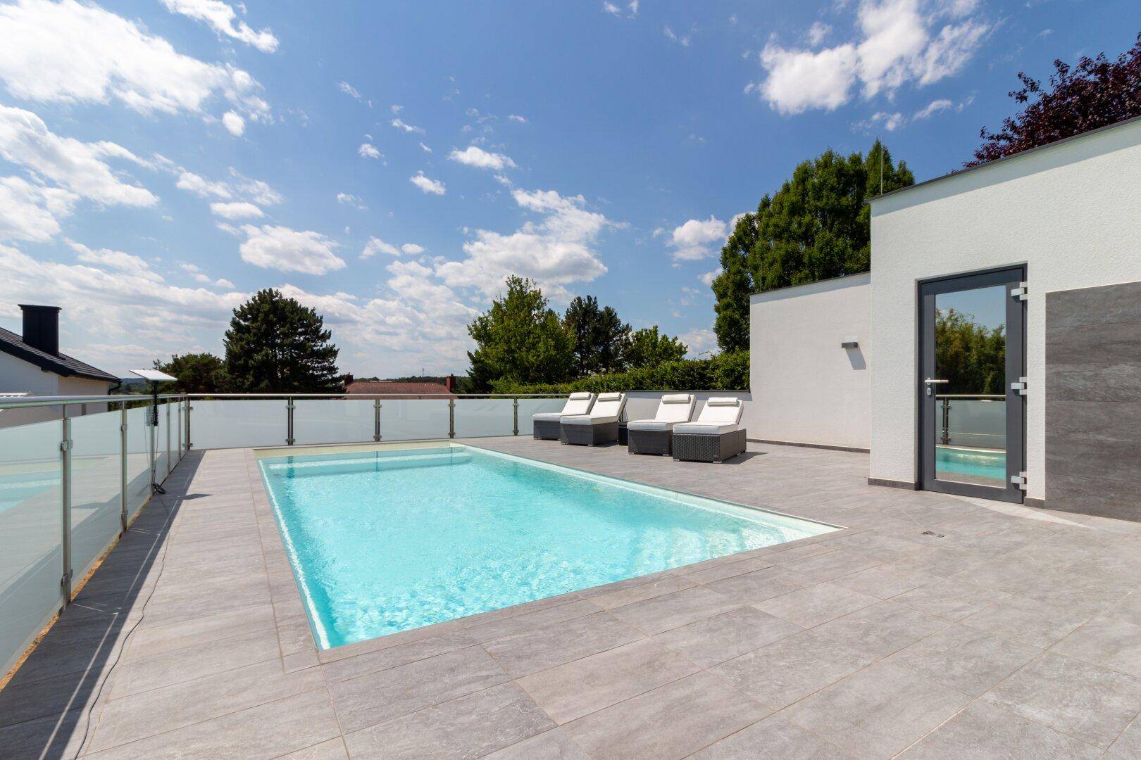 Großer Poolbereich mit Sonnenliegen und weitem Blick über die umliegende Landschaft.