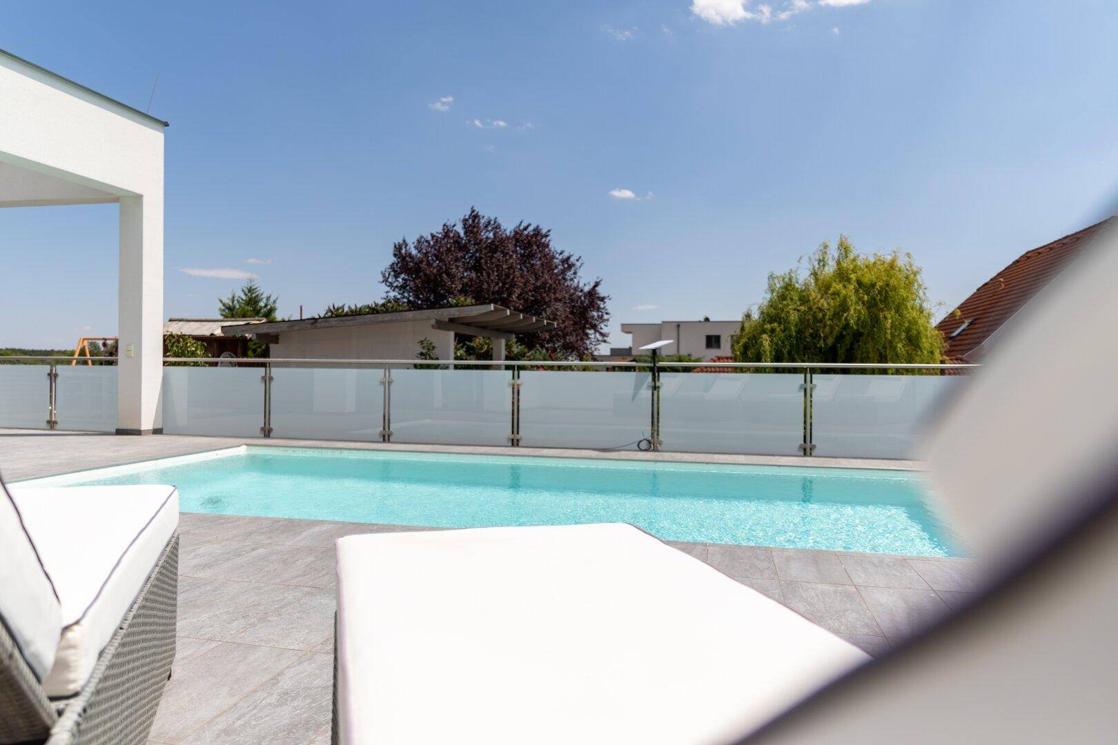 Nahaufnahme des Pools mit Sonnenliegen und einer klaren Sicht auf die Umgebung.