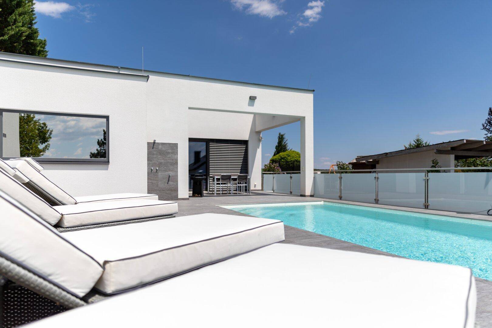 Entspannungsbereich am Pool mit bequemen Sonnenliegen und Blick auf die moderne Architektur.