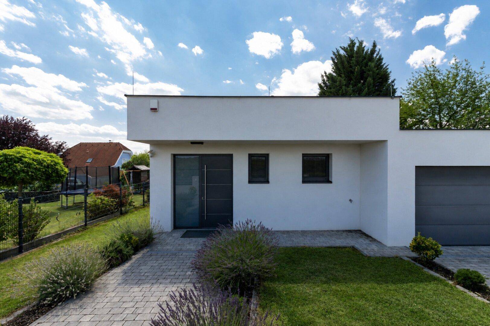 Moderne Hausfassade mit Eingangsbereich, Garagentor und gepflastertem Zugangsweg.