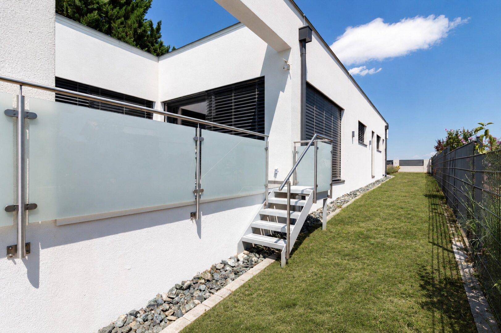 Seitlicher Gartenbereich mit Rasen, Ziersteinen und einer Treppe zum oberen Terrassenbereich.