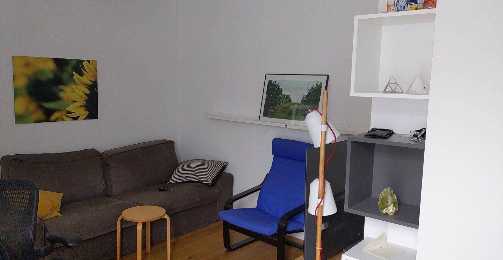 Gemütliches Wohnzimmer mit Sofa, Sessel und einem Bücherregal in neutralen Farben.