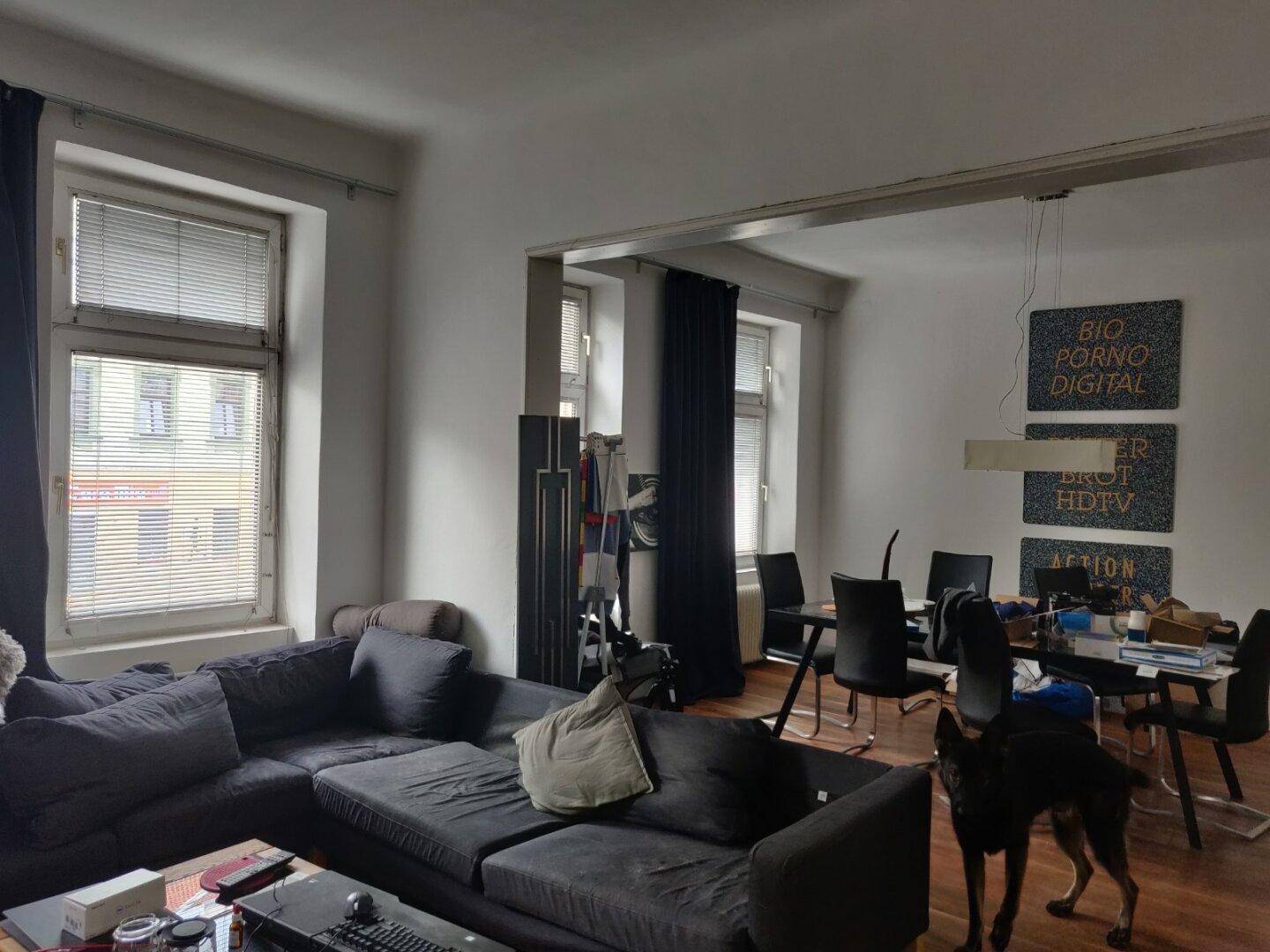 Geräumiger Wohn- und Essbereich mit großem Sofa, Esstisch und mehreren Fenstern.
