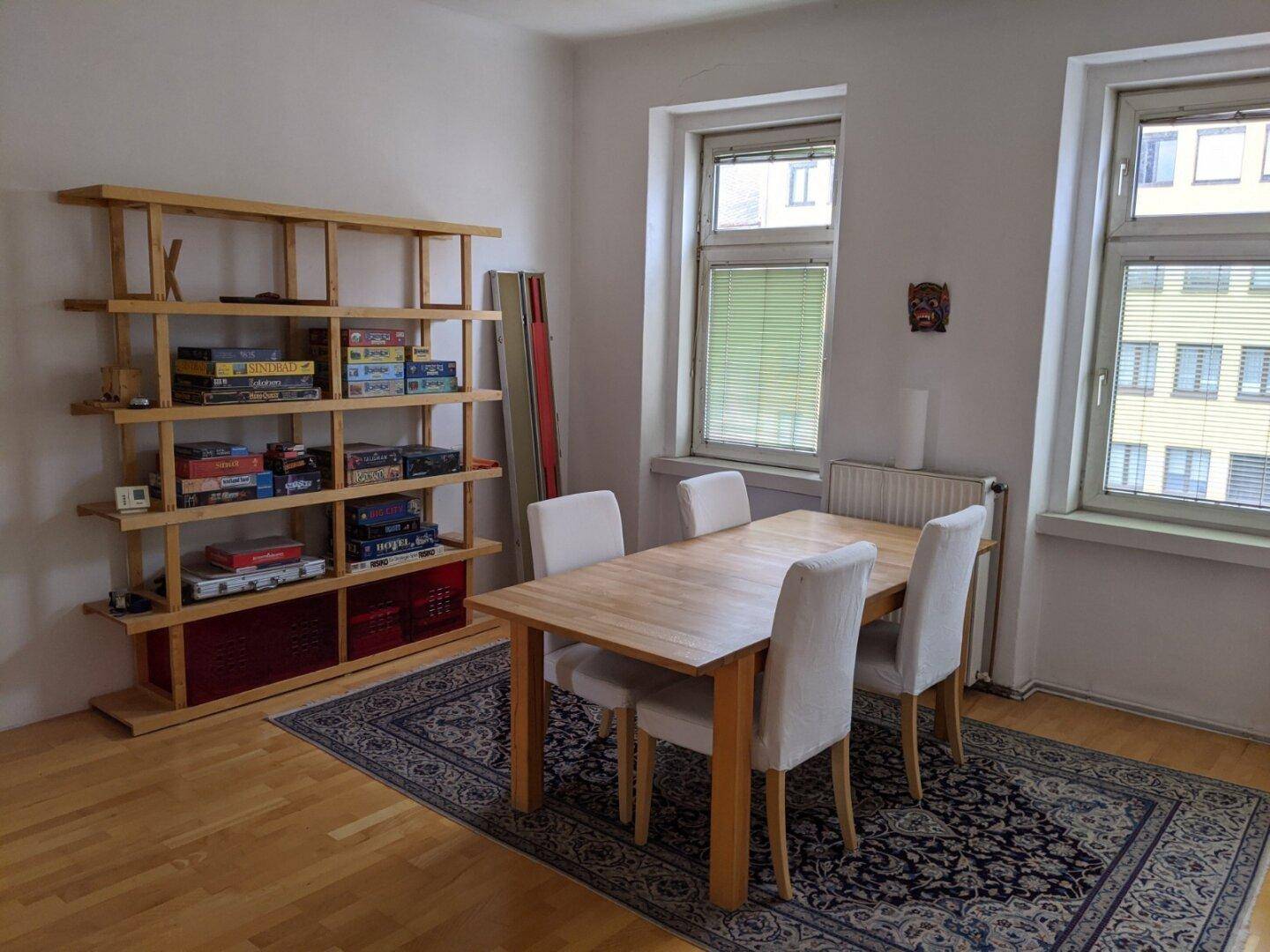 Esszimmer mit Holztisch, vier Stühlen und einem großen Bücherregal.