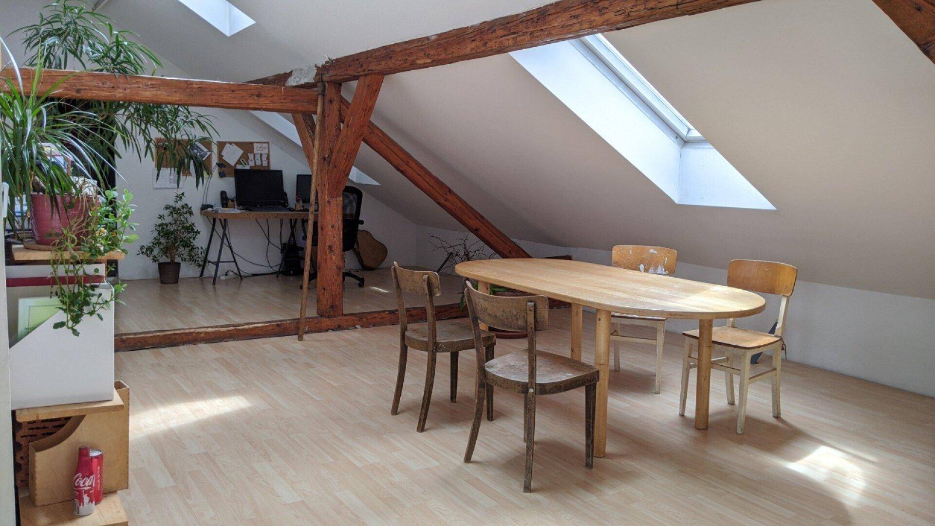 Helles Dachgeschosszimmer mit Holzbalken, Dachfenstern und einem Essbereich.