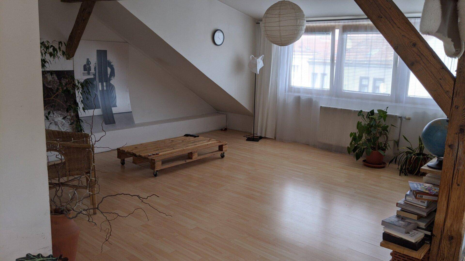 Geräumiges Dachgeschoss-Wohnzimmer mit Holzbalken, großen Fenstern und viel Tageslicht.