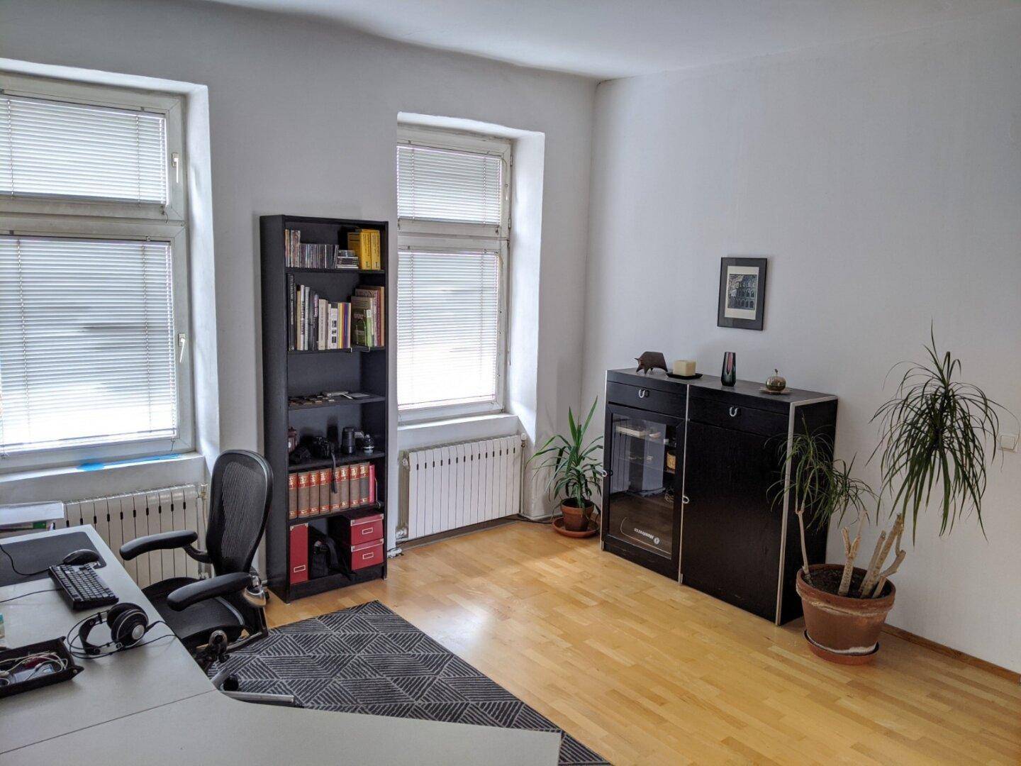 Helles Arbeitszimmer mit Schreibtisch, Bürostuhl und zwei großen Fenstern.