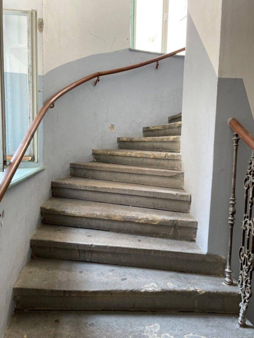 Altes Treppenhaus mit abgenutzten Steinstufen und einem geschwungenen Holzgeländer.