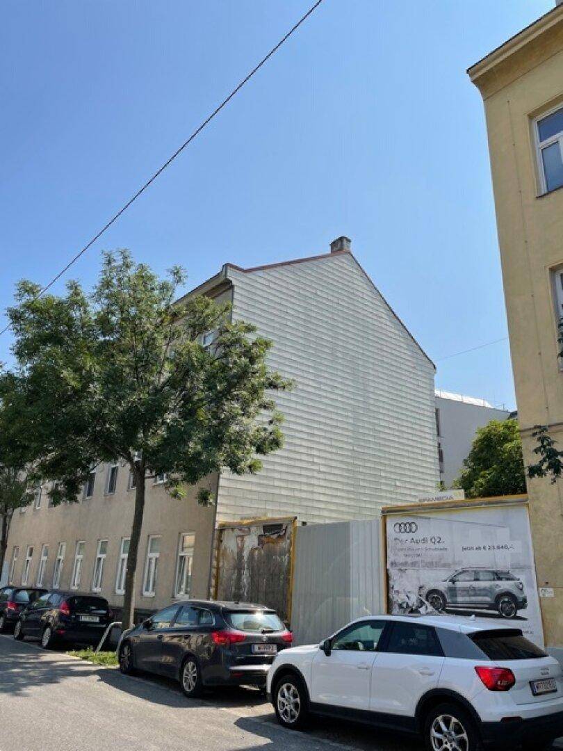 Seitenfassade des Gebäudes mit horizontaler Verkleidung und einer Baustellenabsperrung im Vordergrund.