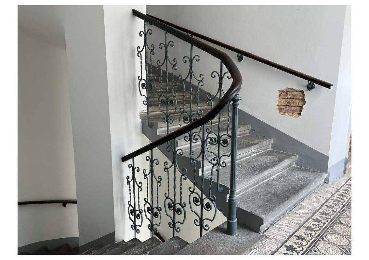 Detailansicht des Treppenhauses mit schmiedeeisernem Geländer und sichtbaren Mauerwerkschäden.