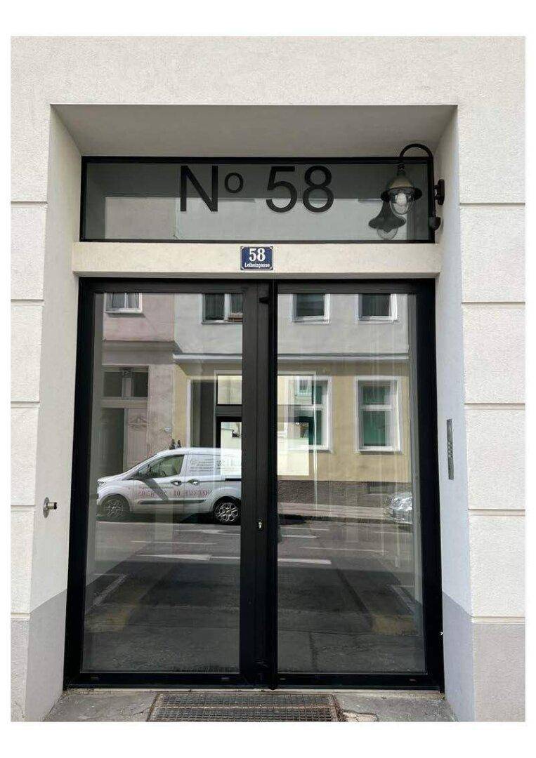 Eingangsbereich eines Gebäudes mit großen Glastüren und der Hausnummer 58.