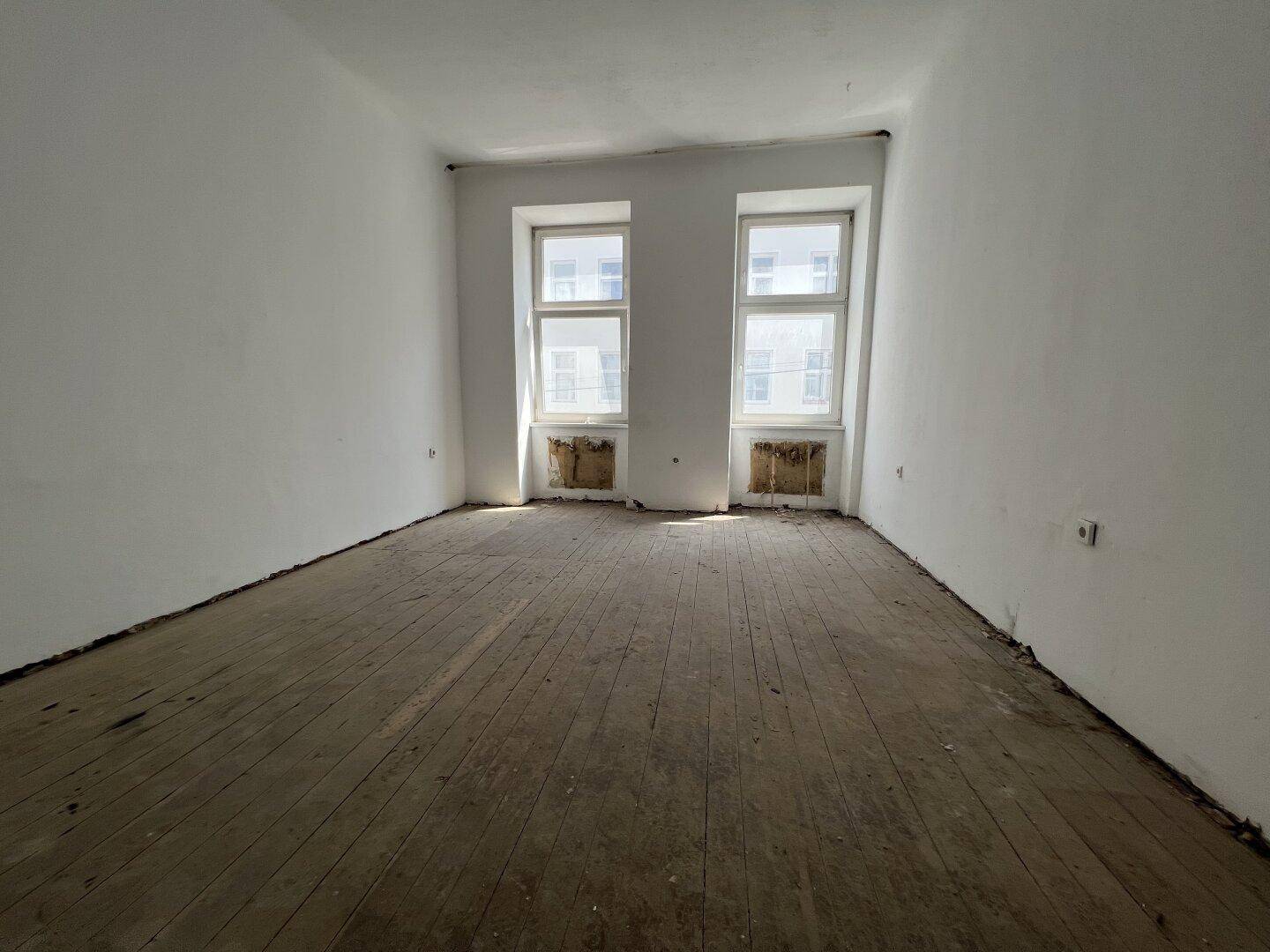 Leerer Raum mit Holzdielenboden und zwei Fenstern, bereit für die Renovierung.