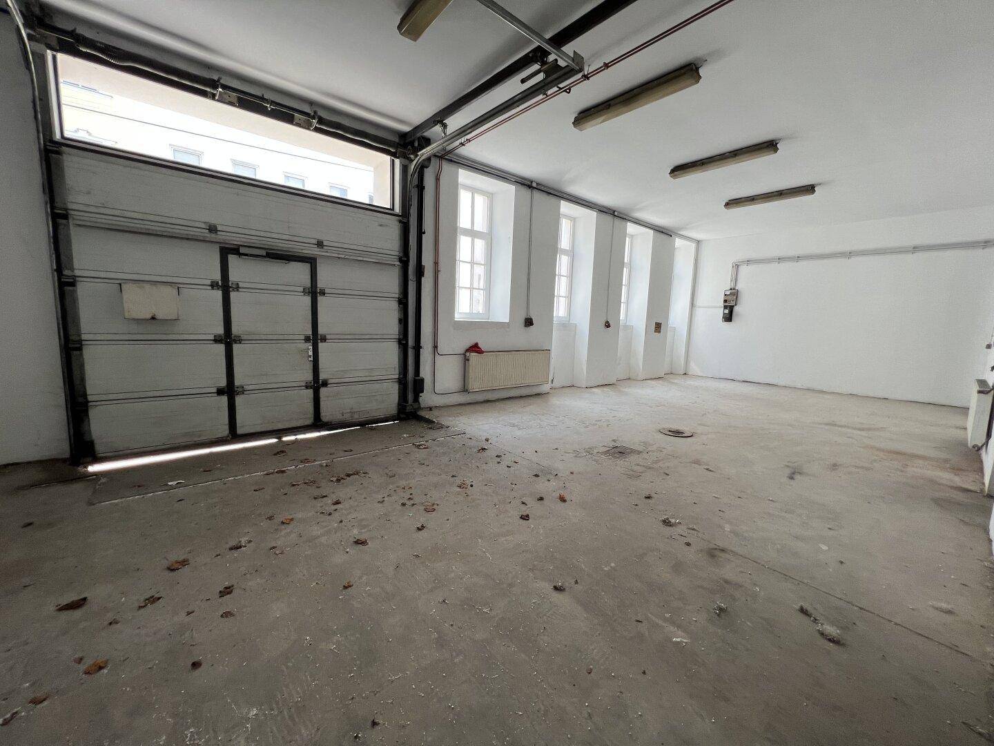 Große leere Garage mit Rolltor und mehreren Fenstern, ideal für Fahrzeuge oder Lagerung.