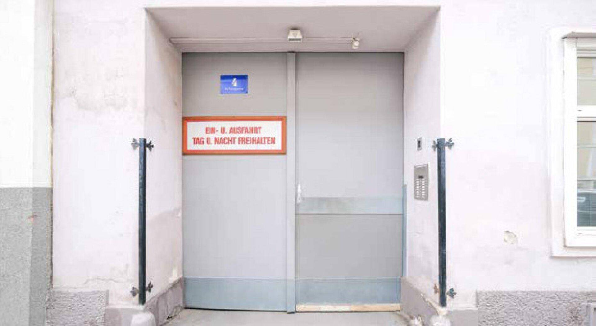 Große graue Einfahrtstür mit Hinweisschild und Gegensprechanlage.