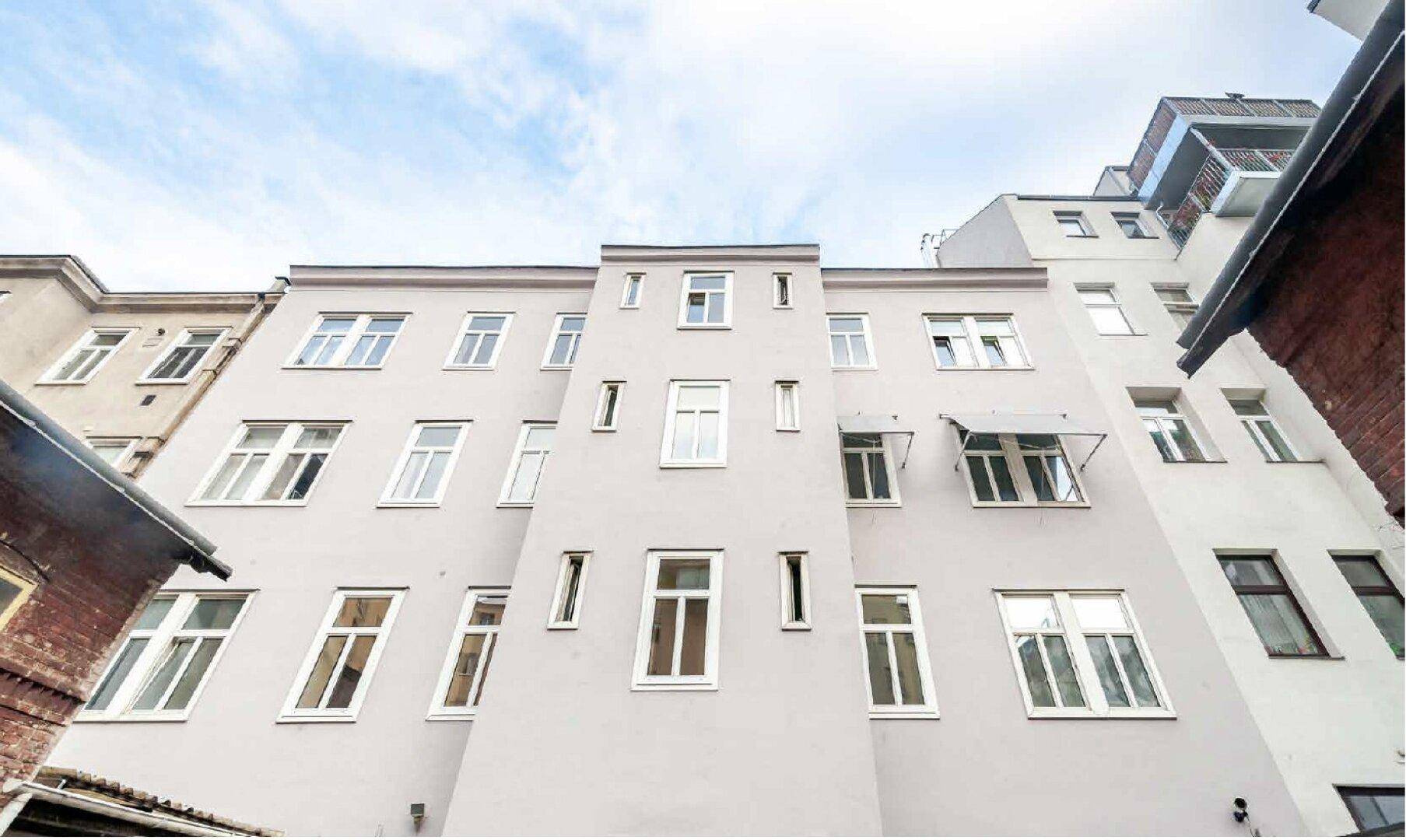 Ansicht der Gebäudefassade von unten mit vielen Fenstern und einem Balkon im oberen Bereich.